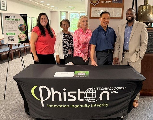 five people standing behind table with tablecloth that says Phiston