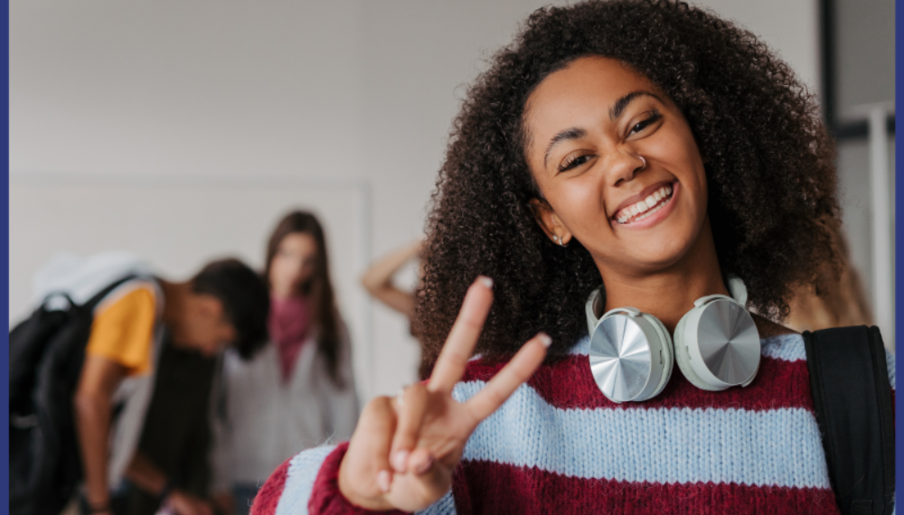 A girl smiles while holding up a peace sign with her hand.