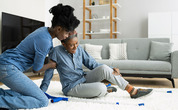 A young woman helps an older woman who is sprawled on the floor after taking a fall.