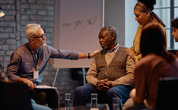 People gather around an older man to lend their support and encouragement during a meeting.