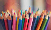 A large collection of colored pencils displayed before a colored background.
