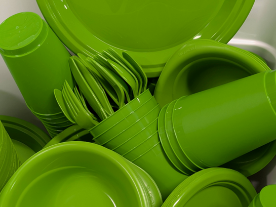 A collection of bright green plastic plates, bowls, cups, and utensils stacked together.
