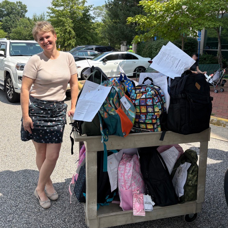 A DFS staff member smiles with a cart full of backpacks for the Adopt-A-Student drive.