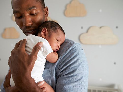 man cradling sleeping newborn