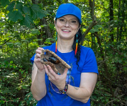 A woman holds up a log with a large beetle on it at a previous Bug Fest.