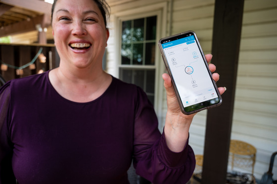 Person standing outside holding up a smartphone displaying an energy monitoring app.