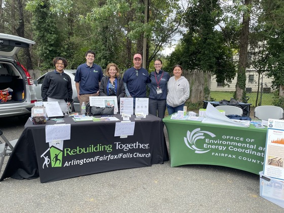 Group standing behind outdoor info tables for Rebuilding Together and Fairfax environmental programs.