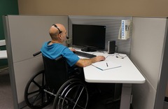 Person using a wheelchair works at a computer station in an office cubicle