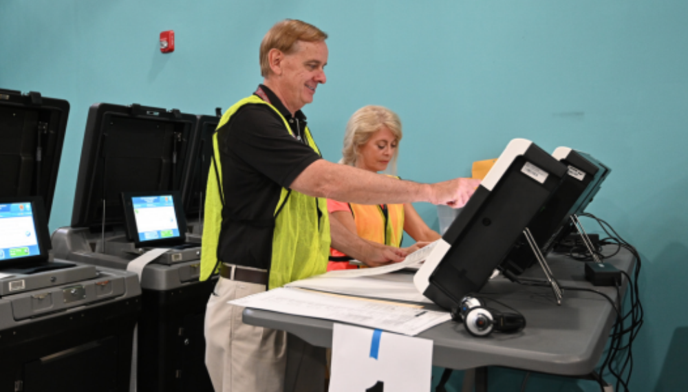 Poll workers operate a ballot scanner. 