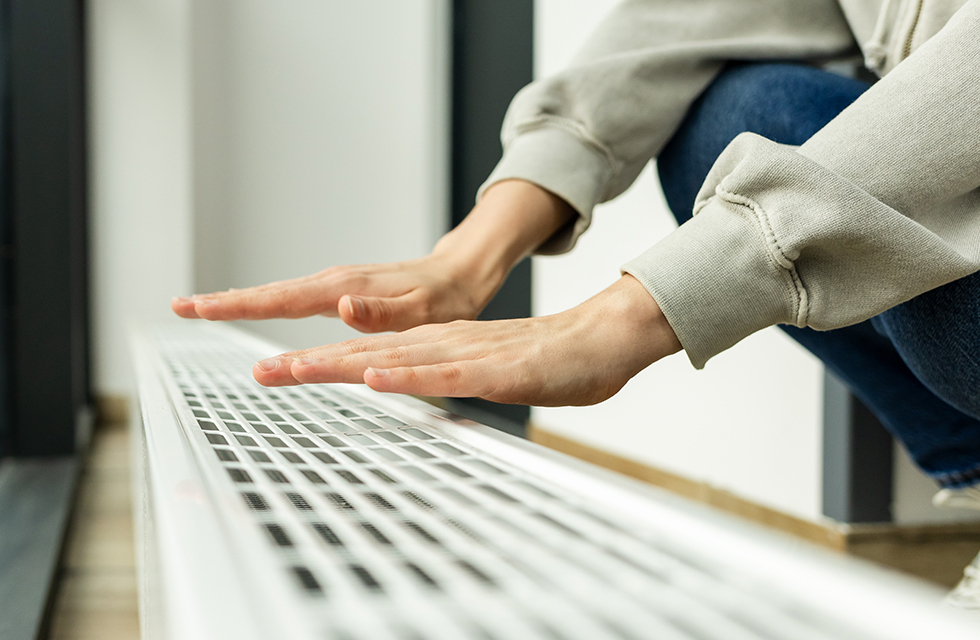 Woman warming hands over heating vent