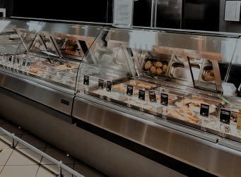 A refrigerated deli counter with meats and other foods displayed behind a clear barrier.