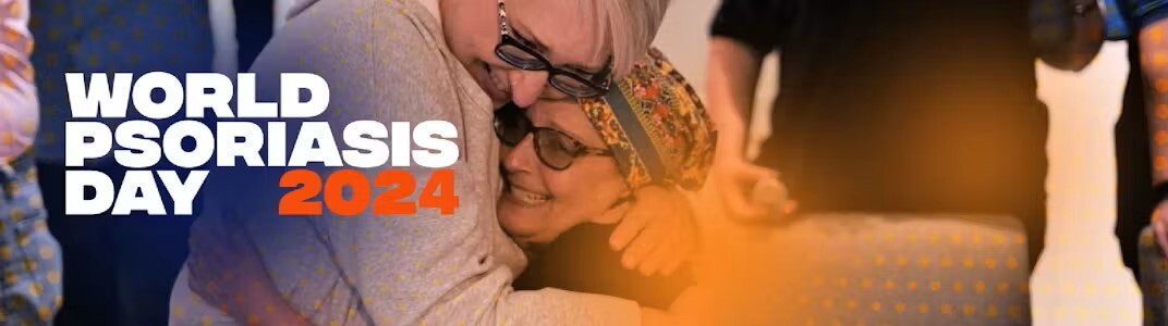 A colorful photo of two people hugging in a room with others and the title World Psoriasis Day 2024 in white and orange text.
