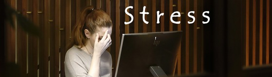 A woman with hand to forehead as with a headache in front of a laptop. The word STRESS appears in white to the side.