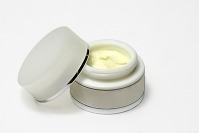 A small jar of light-colored skin cream on a light surface.