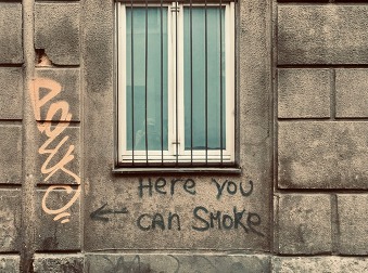 A brick wall and a barred window shown from the outside with the painted message: Here you can smoke.