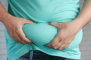 An overweight male in a light turquoise t-shirt squeezes folds of excess belly fat in his two hands.