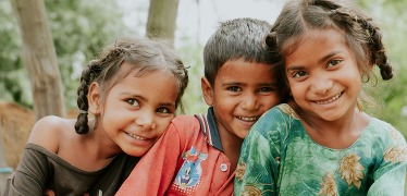 Three kids in colorful clothing lean into each other with big smiles as best friends or siblings.