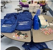 A screenshot of a table at an event with handouts including cloth bags, COVID test kits and other items.