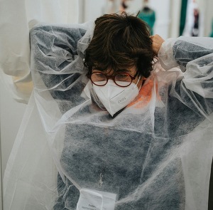A female medical worker in a gown ties a face mask on behind her head.