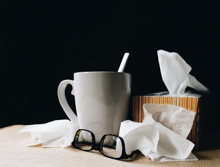 A photo of a cup with spoon, tissue box with used tissues next to it and a pair of glasses.