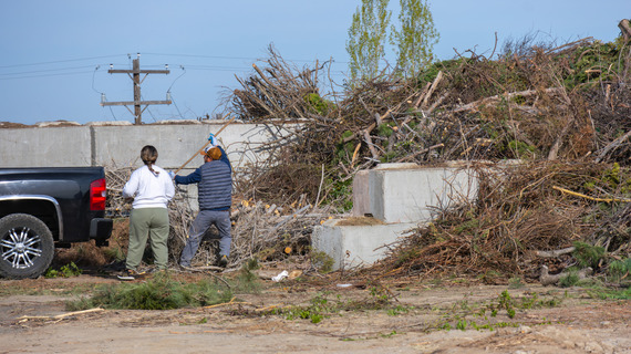 residents moving tree brush from pickup bed to a yard debris pile at the drop-off site