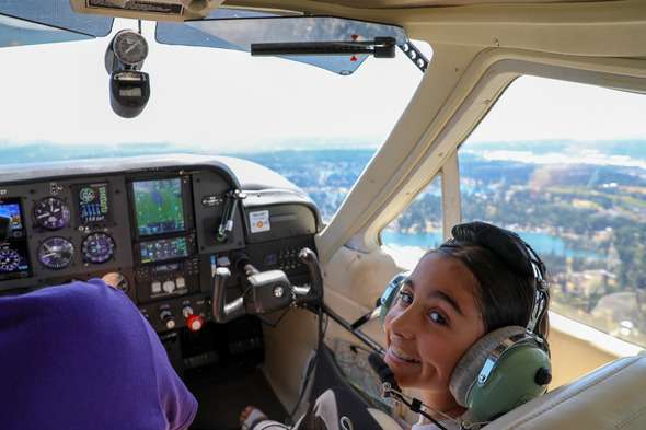 A girl smiling at the camera from the passenger seat of a plane up high in the air at Auburn Airport Day