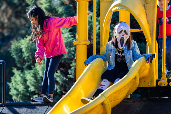 A girl atop a slide wearing a ghost face mask