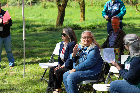 A group of people seated at a tent outside, the sun is shining