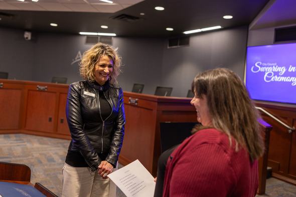 Two women standing in a room, one has her left hand raised