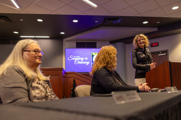 Two women seated at a table while a third stands near a podium nearby 