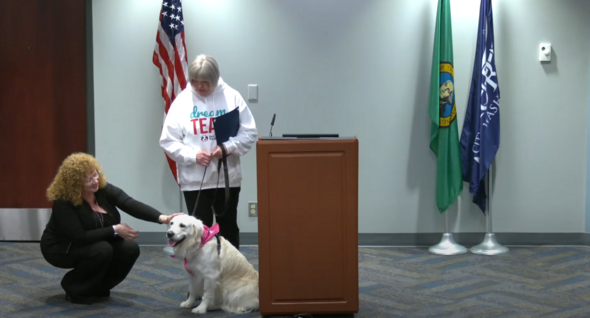 A woman petting a dog while another woman is nearby standing by a podium 