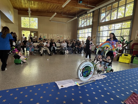 Families watch as children parade decorated strollers and carts at a festive community event.