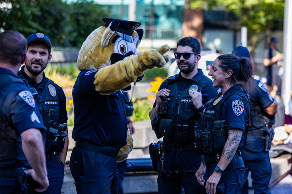 Auburn police officers laughing and talking with a person in a police dog mascot costume during an outdoor event.
