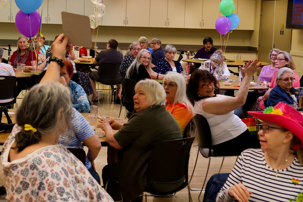 Group of seniors playing bingo at a festive event with balloons and colorful outfits.