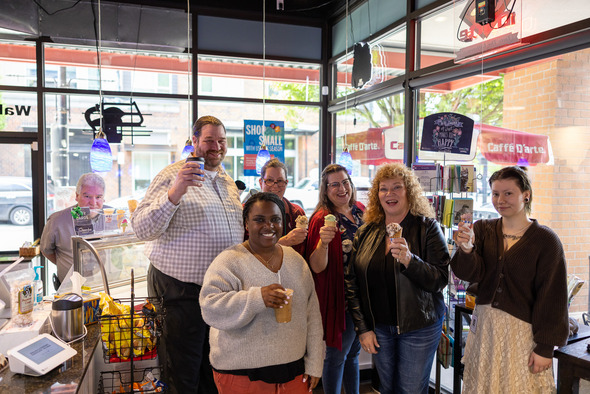 Group of smiling people inside an ice cream shop holding cones and drinks, celebrating together.