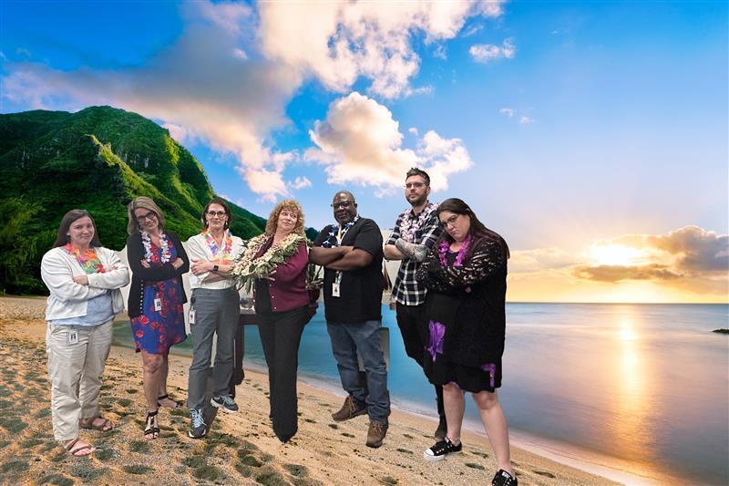 Group of City of Auburn employees posing playfully in Hawaiian shirts and leis with a tropical beach background.