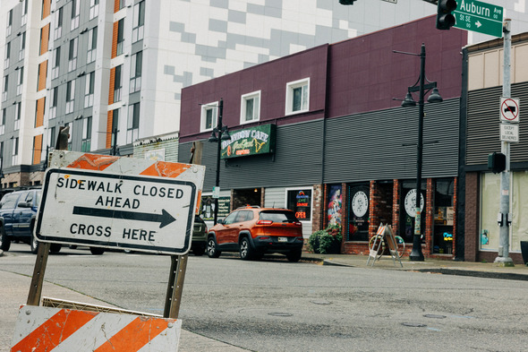 Sidewalk Closed Ahead – Cross Here" sign is posted on a downtown Auburn street corner near the Rainbow Café.