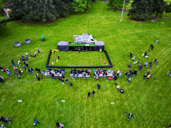 An aerial view shows a large crowd gathered on a grassy field around a fenced stunt dog show at Petpalooza.