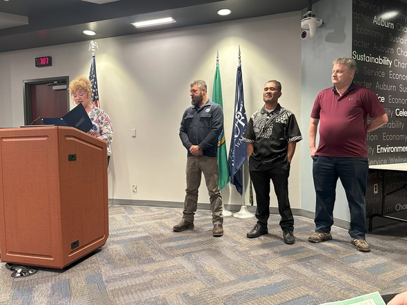 Mayor Nancy Backus reads a proclamation at a podium while four individuals stand beside her during a city ceremony.