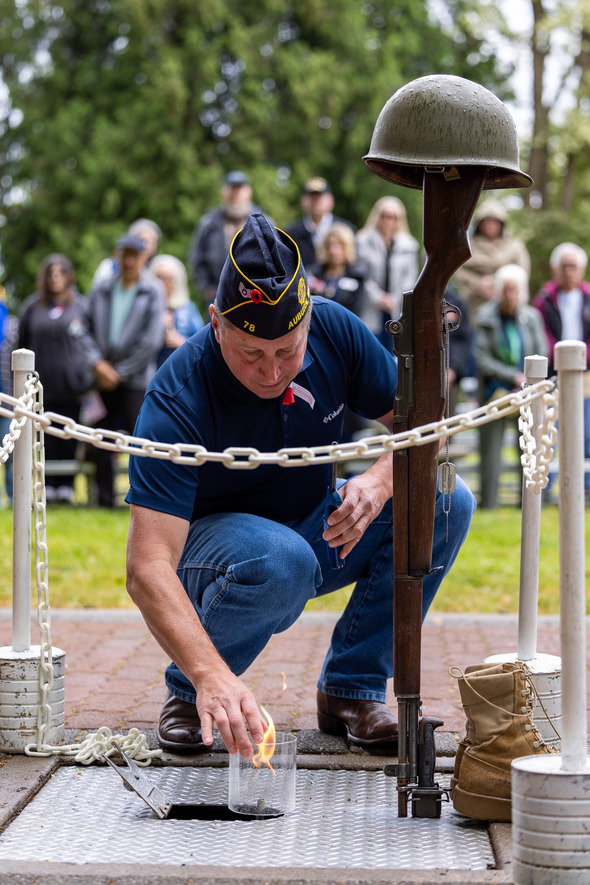 A veteran lights a flame at a battlefield cross memorial during a solemn Memorial Day ceremony, honoring fallen soldiers.