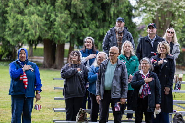 Attendees stand with hands over hearts, holding flags during a Memorial Day ceremony in Auburn, honoring fallen heroes with solemn respect.