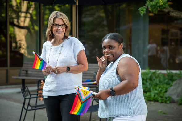 Two women smile and hold Pride flags during an outdoor celebration