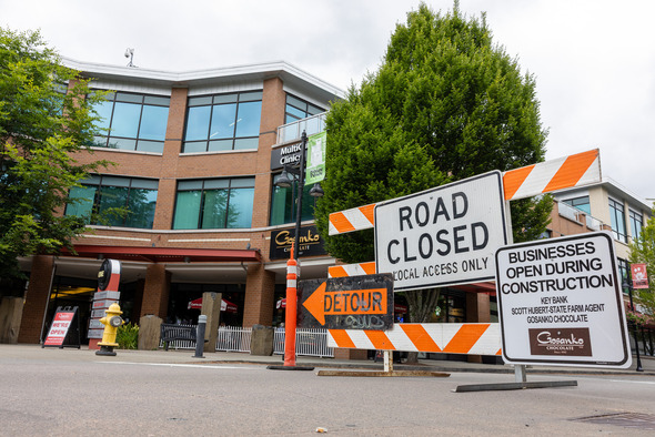 Road closed and detour signs in front of downtown Auburn businesses, with a sign noting businesses remain open during construction