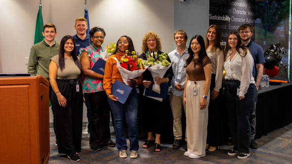 A group of interns and city staff pose with Mayor Nancy Backus, holding flowers and certificates after presentations at Auburn City Hall.