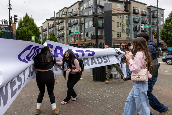 Students laugh and celebrate while holding a large “Congrats West Auburn Grads!” banner downtown.