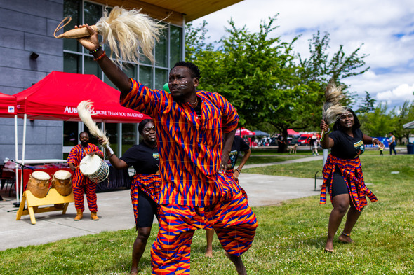 African dancers in colorful clothing perform with drums and traditional props at a Juneteenth celebration.