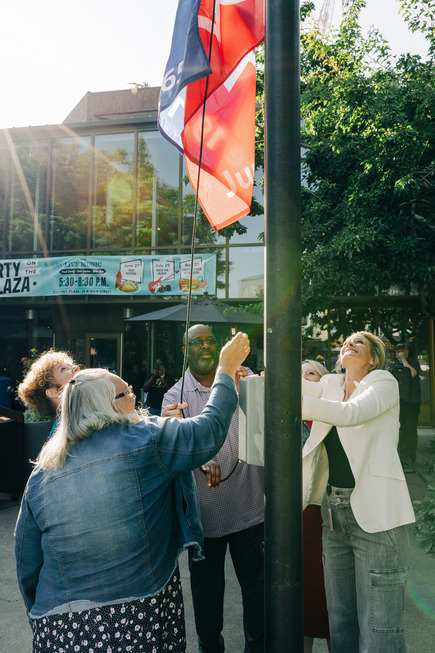 A group raises the Juneteenth flag together outside City Hall, smiling under the morning sun.