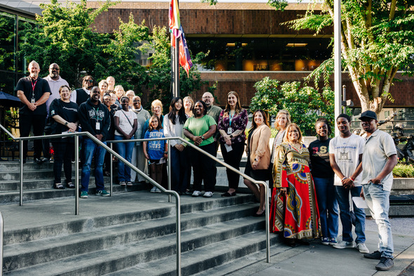 A large group of community members and city staff gather for a photo by the raised Juneteenth flag at City Hall Plaza.