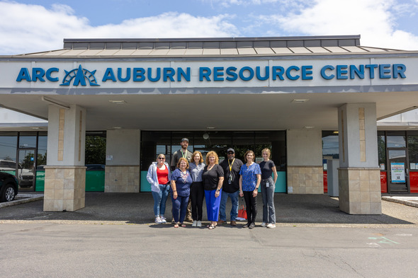 A group of people standing outside the Auburn Resource Center under a large sign.