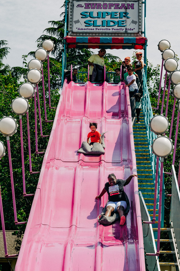 Kids and adults sliding down a bright pink slide at a carnival ride called the "European Super Slide